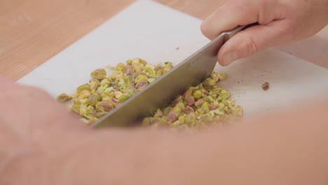 Close-up-of-hands-chopping-pistachios-on-a-cutting-board,-in-slow-motion