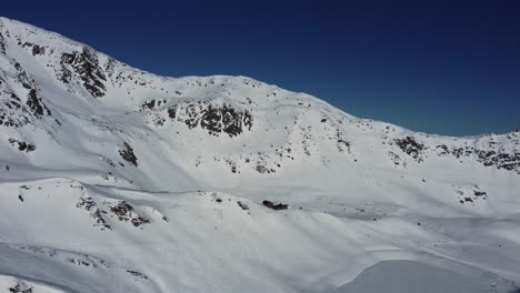 Remote-cabin-in-white-snowy-mountains-in-Alps,-aerial