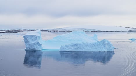 Blue-Antarctica-Iceberg-and-Ice-in-Calm-Sea-Water,-Reflections-in-Still-Flat-Ocean,-Beautiful-Big-Large-Icebergs-in-Coastal-Winter-Scene,-Amazing-Shapes-on-Antarctica-Peninsula-in-Dramatic-Scenery