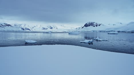 Paisaje-Invernal-Con-Océano-Nevado-Y-Montañas-En-La-Antártida,-Icebergs-En-El-Mar-En-Un-Hermoso-Y-Dramático-Paisaje-Marino-Costero-Azul-Oscuro-En-La-Costa-De-La-Península-Antártica,-Escena-Helada-Del-Mar-Invernal-Con-Hielo