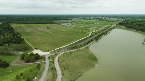 Shelby-farms-park-in-memphis-with-lush-greenery,-water-body,-and-walking-paths,-on-a-cloudy-day,-aerial-view