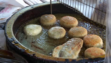 Delicious-Xian-Bing-cooking-in-the-pan,-a-stall-vendor-flipping-savoury-minced-pork-meat-pie-pastry,-deep-fried-until-golden-brown-with-a-crispy-outside,-close-up-shot-of-popular-Taiwanese-street-food