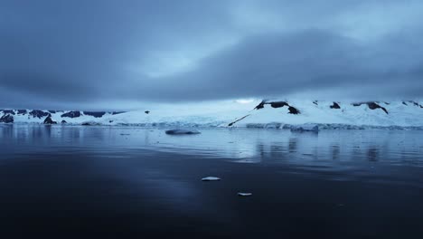 Luftaufnahme-Einer-Drohne-Aus-Der-Antarktis-Mit-Bergen-Und-Gletschern-Mit-Dramatischen-Blauen-Wolken,-Wunderschöne-Landschaft-Der-Antarktis-Halbinsel-Auf-Dem-Südlichen-Ozean-Mit-Ruhigem,-Noch-Flachem-Wasser-Mit-Spiegelungen