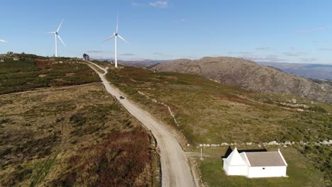 Car-Traveling-in-Mountain-Road-With-Wind-Turbine-Aerial-View