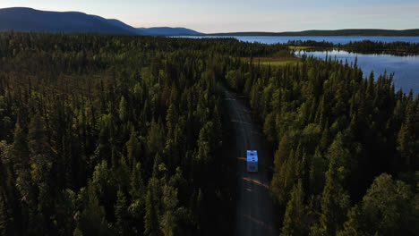 Drone-following-a-caravan-driving-close-to-lake-Pallasjarvi,-summer-in-Lapland
