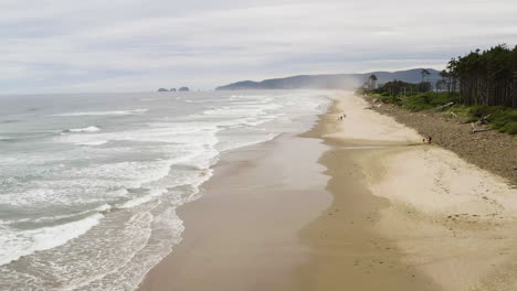 Aerial-dolly-along-gentle-crashing-waves-on-wide-sandy-beach-of-Cape-Lookout-Oregon