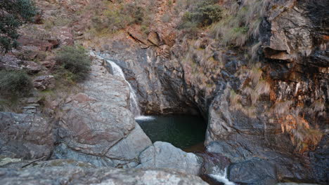 Abgeschiedene-Wasserfall-Oase-Zwischen-Schroffen-Klippen-In-Der-Abenddämmerung,-Luftaufnahme