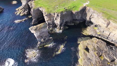 Aerial-View-of-Birds-Flying-Above-Sea-Stack-and-Picturesque-Coastline-of-Scotland-on-Sunny-Day,-Drone-Shot