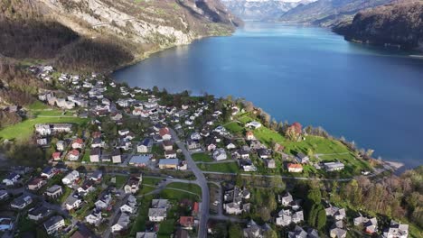 Vista-Aérea-De-Weesen,-Suiza,-Con-Encantadoras-Casas-Agrupadas-A-Lo-Largo-De-Las-Orillas-Del-Resplandeciente-Walensee,-Enmarcadas-Por-Verdes-Colinas.