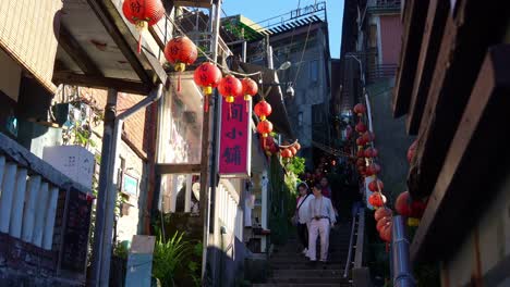 People-walking-down-the-narrow-steep-staircases,-exploring-the-charming-Jiufen's-Old-Street-mountain-village-town-with-shops-and-food-stalls-along-the-way