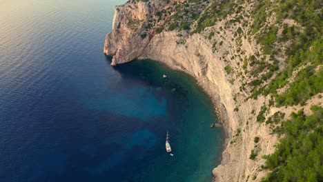 Ibiza-sailboat-seaside-cliff-basking-in-warm-glow-of-sunset