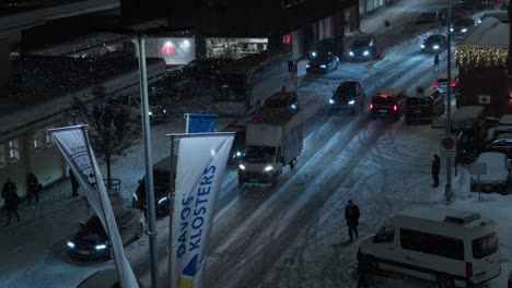 High-angle-night-time-shot-showing-traffic-leaving-Davos-during-the-World-Economic-Forum,-Davos-Klosters-banners-are-visible-and-people-are-walking-through-the-streets