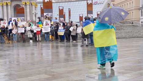 Child-wrapped-in-Ukranian-blue-and-yellow-flag-walks-across-rainy-grounds-in-Capitol