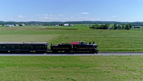 A-classic-locomotive-pulls-carriages-across-verdant-fields-under-a-clear-blue-sky