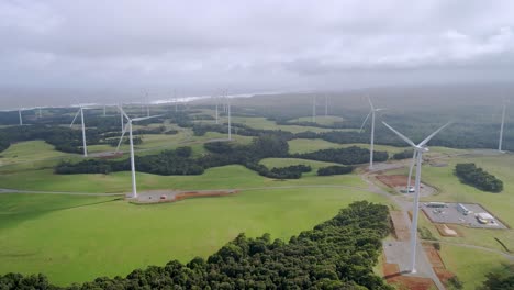 Drone-tilt-shot-of-renewable-energy-wind-farm-with-spinning-turbines-on-cloudy-day-on-Tasmania's-west-coast,-Australia