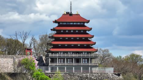 Rote-Mehrstöckige-Pagode-Mit-Traditioneller-Ostasiatischer-Architektur,-Vor-üppigen-Bäumen-Und-Einem-Bewölkten-Himmel