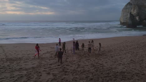 Group-of-happy-people-dancing-on-sandy-beach-in-Portugal-after-sunset-time