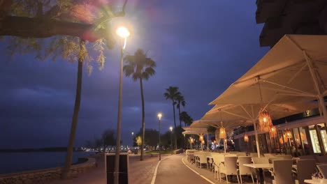 Noche-En-Cala-Bona,-Mallorca-Paseo-Marítimo-Bien-Iluminado-Cerca-Del-Mar-Y-Terrazas-De-Un-Restaurante.