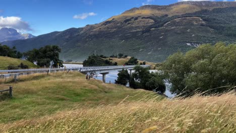 Mann-Läuft-An-Einem-Windigen-Tag-über-Eine-Brücke,-Mit-Bergen-Und-Blauem-Himmel,-Neuseeland