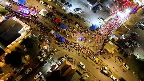 Drone-bird's-eye-view-above-parade-at-night-with-dancers-rounding-bend-in-street