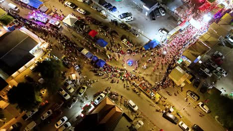 Vista-Aérea-De-Drones-Sobre-El-Desfile-Nocturno-Con-Bailarines-Doblando-Una-Curva-En-La-Calle