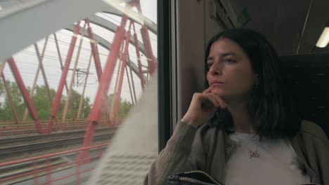 Woman-thinking-deeply-on-a-train-passing-red-bridge