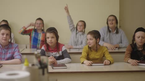 ultra--Orthodox-Jewish-students-with-a-kippahs-lerning-in-class-holding-their-hands-up