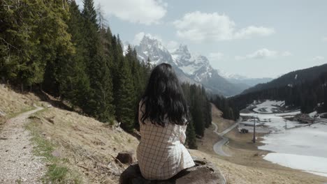 Mujer-Joven-Sentada-En-El-Tocón-De-Un-árbol-En-Las-Montañas-Con-Vistas-A-Los-Alpes-Dolomitas-En-Italia