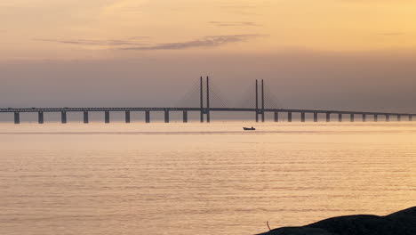 A-Beautiful-Shot-Of-Oresund-Bridge-With-A-Boat-Alone-In-The-Water-At-Golden-Hour---Malmo,-Sweden