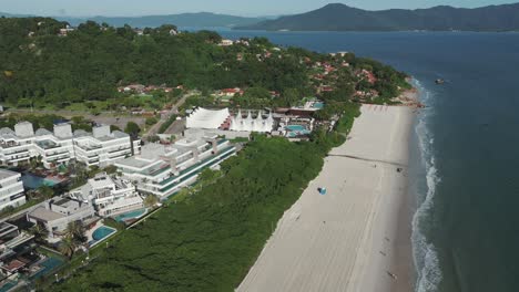 Aerial-view-showcases-the-expanded-sandy-shores-of-Jurerê-Internacional-Beach,-situated-on-the-northern-coast-of-Florianopolis-Island,-Brazil