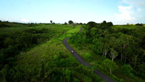 Girl-in-white-drives-scooter-uphill-while-exploring-Teletubbies-Hills,-Bali