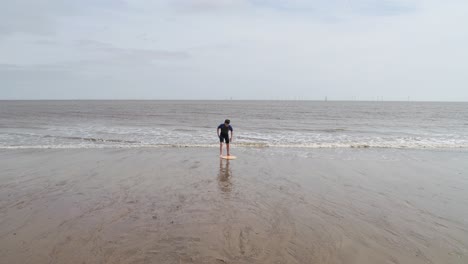 Young-boy-in-a-wetsuit-on-a-beach-digging-in-the-sand