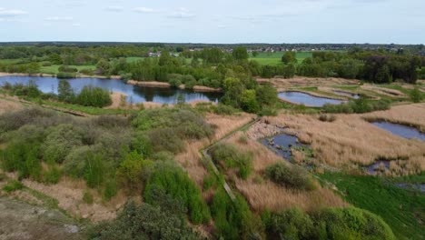 Vista-Aérea-Sobre-El-Paisaje-Del-Norte-De-Bélgica-Con-Lagos-Y-Bosques-Con-La-Ciudad-En-La-Distancia