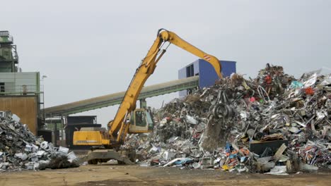 Excavator-managing-a-large-pile-of-mixed-scrap-metal-at-a-recycling-plant-during-the-day