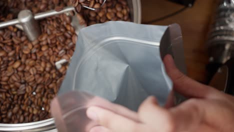 Person-pouring-spoonfuls-of-roasted-coffee-beans-into-a-bag-for-export