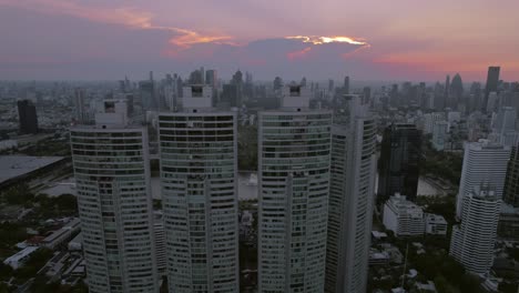 High-rise-apartment-buildings-in-Bangkok-at-sunset,-twilight,-reversing-drone