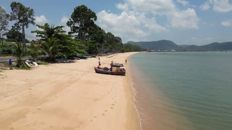 Fishing-boat-on-wide-sandy-beach-of-Bang-Saray-with-man-enjoying-sunshine-and-walk-near-the-Gulf-of-Thailand