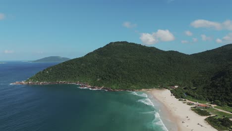 Die-Luftaufnahme-Zeigt-Die-Herrliche-Brasilianische-Küste-Mit-Kristallklarem-Grünem-Wasser-Und-üppigen-Bergen,-Die-Von-Dichtem-Dschungel-Geschmückt-Sind