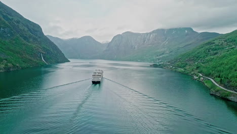 Cruise-ship-in-a-deep,-narrow-fjord-in-Norway---pullback-aerial-revealing-the-rugged-landscape