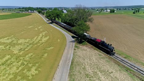 A-historic-steam-locomotive-powers-along-the-tracks,-past-golden-fields,-under-a-clear-blue-sky