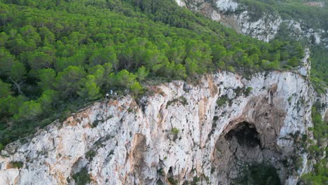 Hikers-rest-on-a-rocky-cliff-among-trees-with-a-view-of-the-green-landscape-during-sunset-in-ibiza