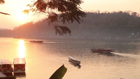 golden-glow-of-sunset-reflecting-on-the-mekong-river-with-boats-floating-in-Luang-Prabang,-Laos-traveling-Southeast-Asia
