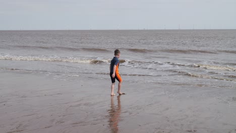 Young-boy-in-a-wetsuit-on-a-beach-digging-in-the-sand