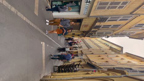 Tourists-and-locals-stroll-on-charming-street-in-Aix-en-Provence,-France,-sidewalk-cafe-nearby,-daytime