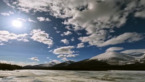 Timelapse-of-a-frozen-river-against-the-backdrop-of-mountains-and-floating-sunny-clouds