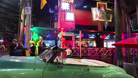 Vibrant-nightlife-scene-at-El-Poblado,-Medellin-with-a-classic-car-in-the-foreground