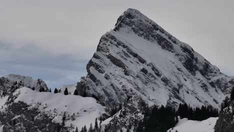 Circling-Drone-Shot-of-Large-Mountain-Peak-Covered-in-Thin-Blanket-of-Snow,-Wintertime