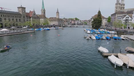 Disparo-De-Dron-En-Movimiento-Lento-Que-Muestra-Una-Fiesta-En-Un-Muelle-Y-Muestra-La-Arquitectura-Del-Casco-Antiguo-Siguiendo-El-Río