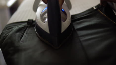 Close-up-of-an-individual-ironing-a-pair-of-black-trousers-using-a-flat-iron-on-an-ironing-board