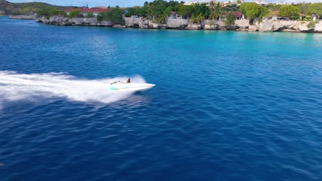 Speedboat-bounces-as-it-races-flying-across-open-ocean-surface-by-scenic-cliffs